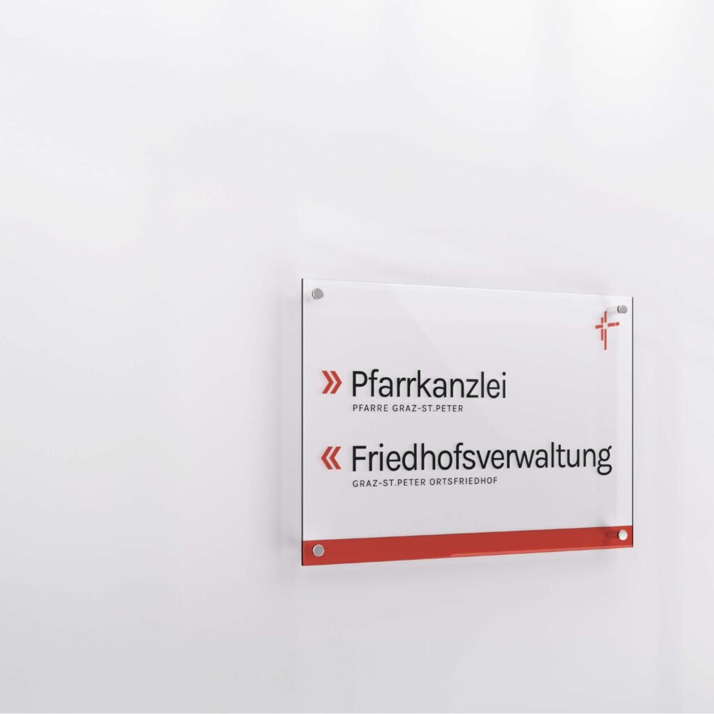 Acrylschild an weißer Wand mit Aufschrift „Pfarrkanzlei“ und „Friedhofsverwaltung Graz-St. Peter“, ergänzt durch rote grafische Elemente.