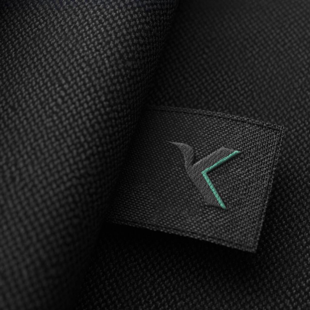 Gesticktes schwarzes Label mit stilisiertem „K“-Logo auf strukturiertem Stoff – hochwertiges Branding für Sport- und Fitnessbekleidung.