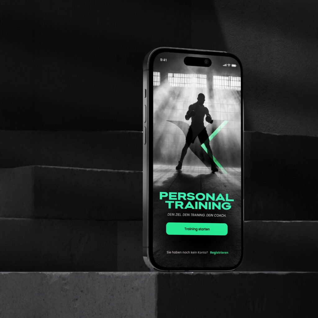 Smartphone steht auf Betontreppe; Display zeigt Personal-Training-App mit Slogan „Dein Ziel. Dein Training. Dein Coach.“ und einem sportlichen Schattenbild.
