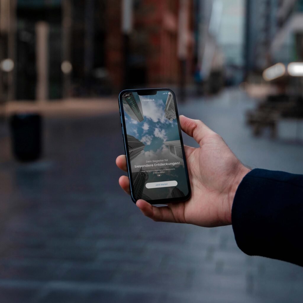 Hand hält Smartphone mit Trawalk-App; Display zeigt Spiegelung von Hochhäusern und Himmel in städtischer Umgebung.