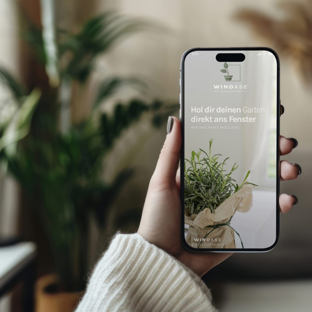 Smartphone mit geöffneter Windase-App wird in der Hand gehalten – Pflanzen im Hintergrund, natürliche Szene in Innenraum