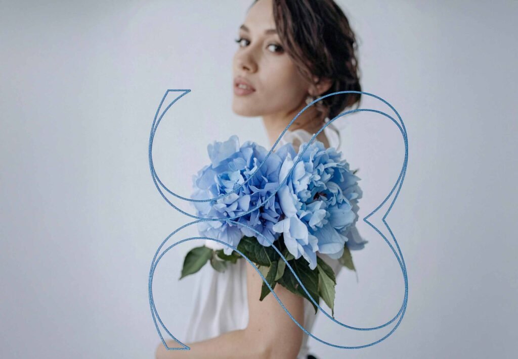 Portrait einer Frau mit blauer Blüte vor hellem Hintergrund, ergänzt durch Ornamentlinie – visuelles Keymotiv für Editorial-Kampagne