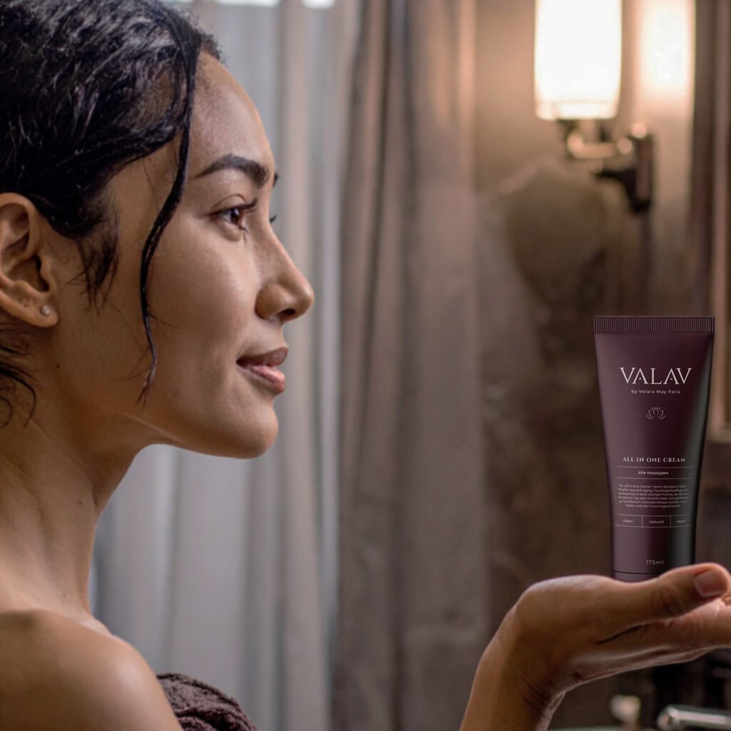 Nahaufnahme einer Frau mit dunklem Haar, die in einem Badezimmer eine Tube VALAV All in One Cream in der Hand hält, warme Beleuchtung, luxuriöse Hautpflege-Szene.