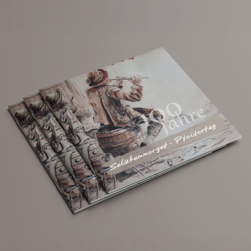 Gestapelte Booklets zum 100-jährigen Pfeifertag mit Illustration von zwei Musikanten.