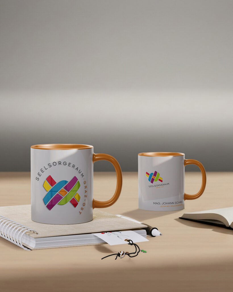 Personalisierte Kaffeetassen mit Logo des Seelsorgeraums Graz auf Schreibtisch arrangiert