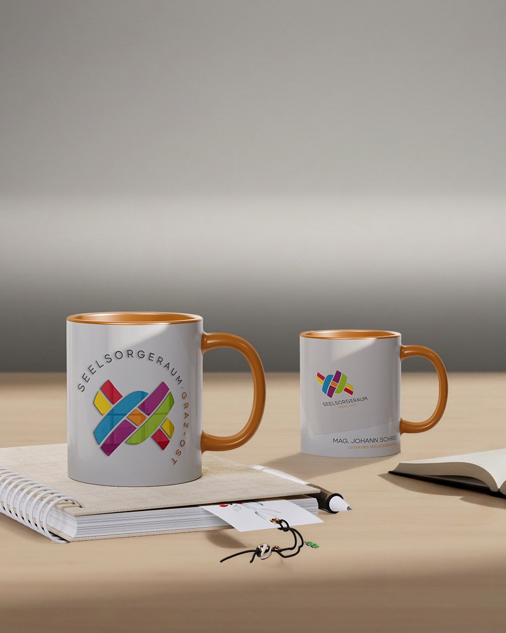 Personalisierte Kaffeetassen mit Logo des Seelsorgeraums Graz auf Schreibtisch arrangiert
