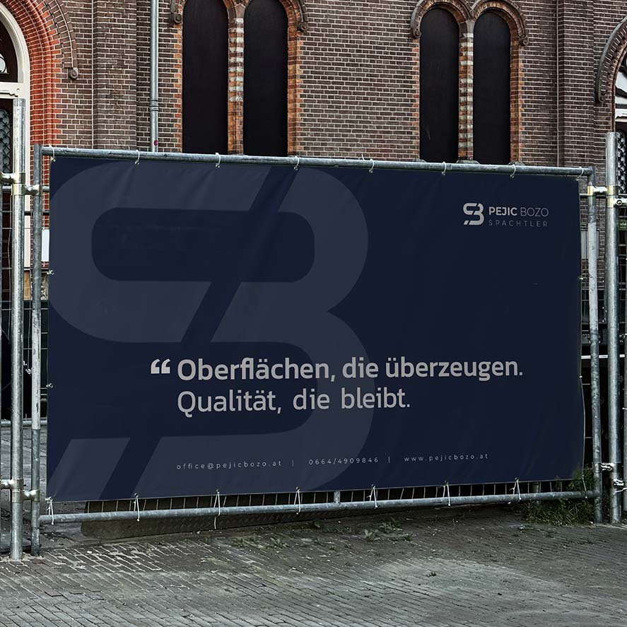 Dunkelblaues Bauzaunbanner von Pejic Bozo Spachtler mit großem SB-Logo und Slogan „Oberflächen, die überzeugen. Qualität, die bleibt.“ vor Backsteinfassade.