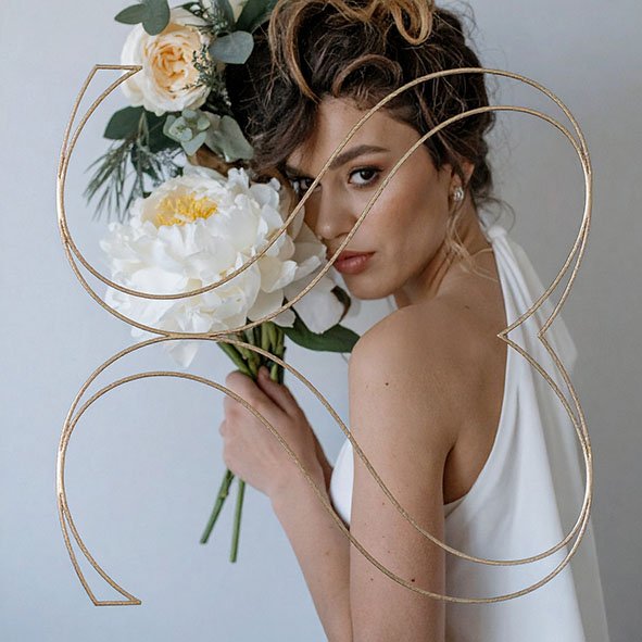Braut mit weißem Blumengesteck und goldenem „B“-Logo vor hellem Hintergrund