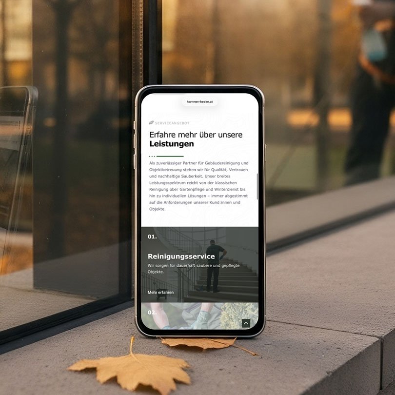 Smartphone mit geöffneter Website von Hammer & Hecke, Reinigungsservice, mobiloptimiertes Design auf Herbsthintergrund