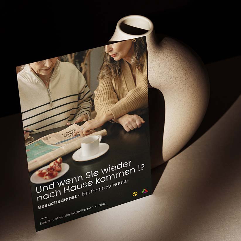 Plakat auf Tisch gelehnt, zeigt emotionales Bildmotiv und Text zur Nachsorge-Initiative "Und wenn Sie wieder nach Hause kommen!?"