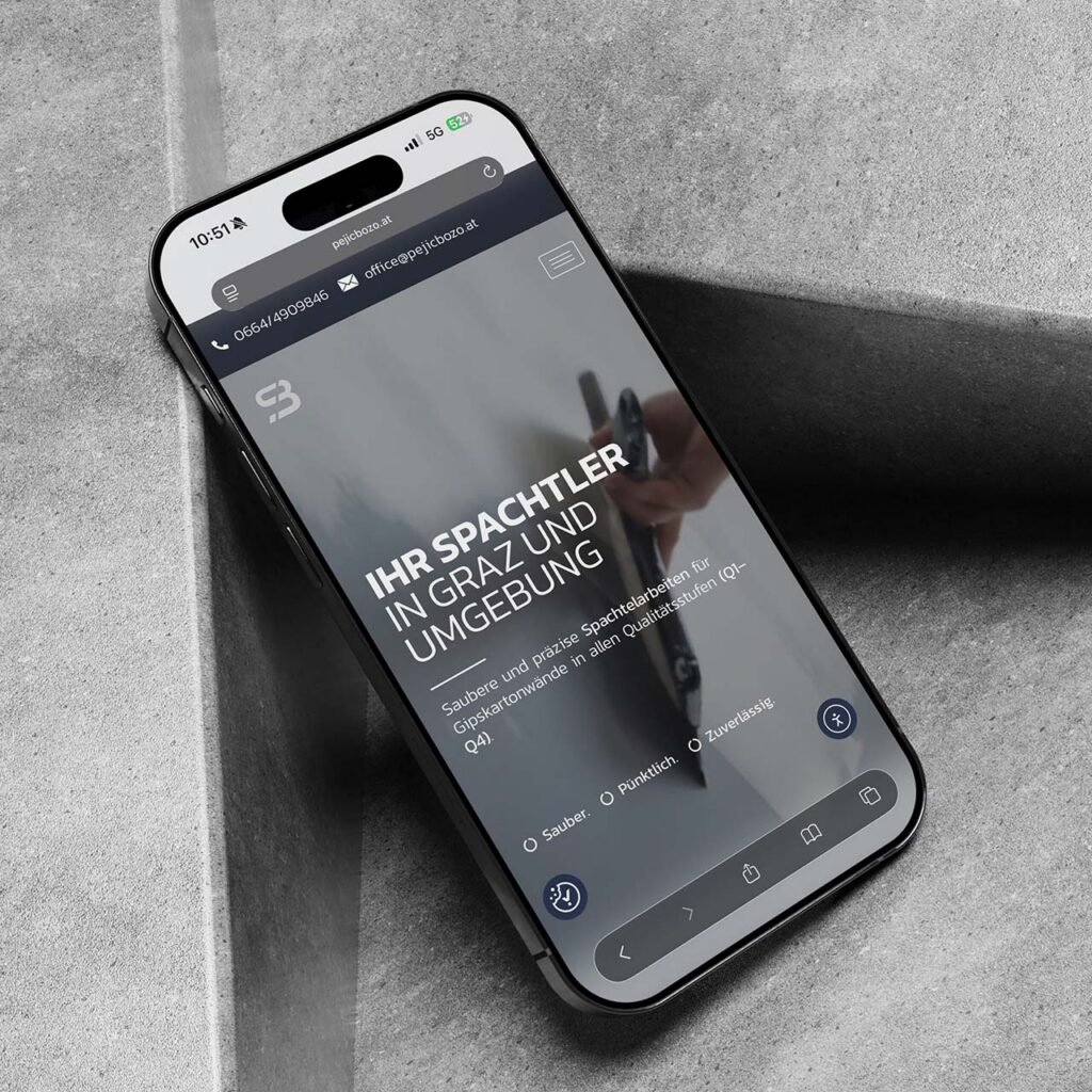 Smartphone mit der mobilen Website von Pejic Bozo Spachtler – zeigt den Startbildschirm mit Slogan „Ihr Spachtler in Graz und Umgebung“ auf modernem Betonhintergrund.