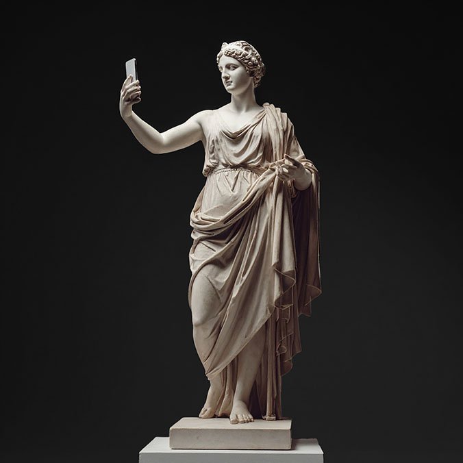 Statue einer klassischen griechischen oder römischen Frau, die ein Selfie mit einem Smartphone macht – modernes Kunstwerk mit historischem Bezug.