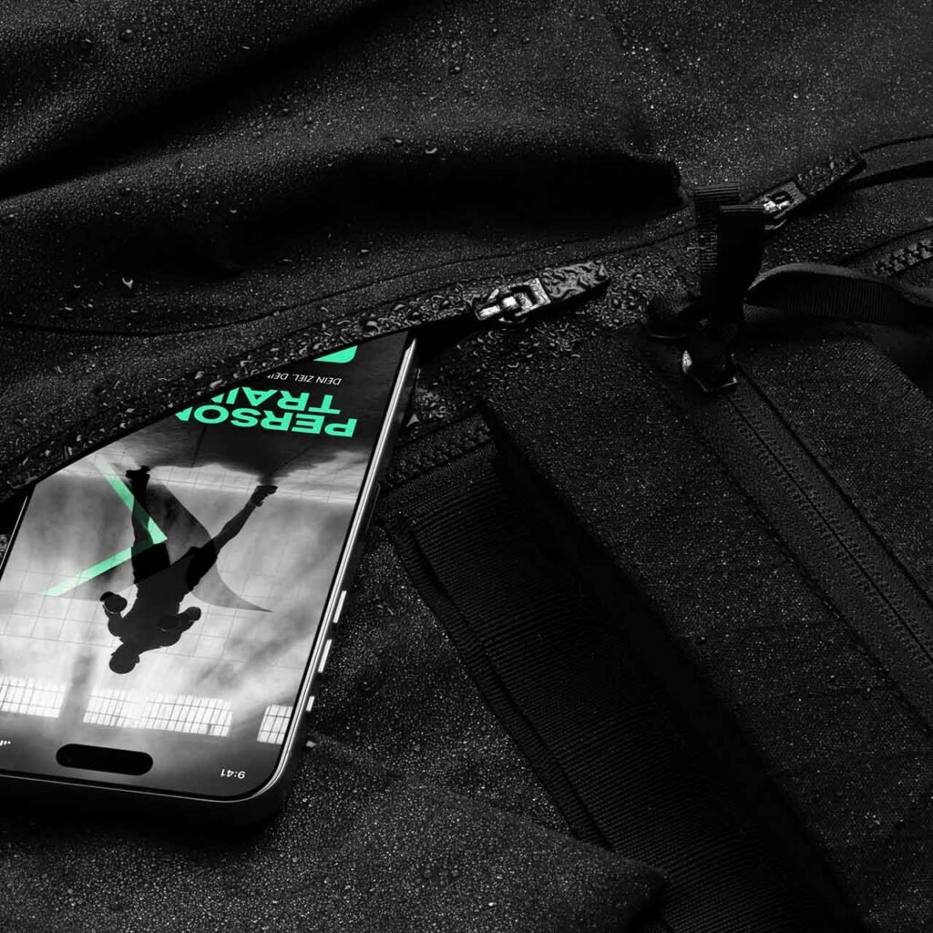 Smartphone mit „Personal Training“-Display ragt aus geöffneter schwarzer Sporttasche – modernes Fitnessbranding in Alltagssituation.