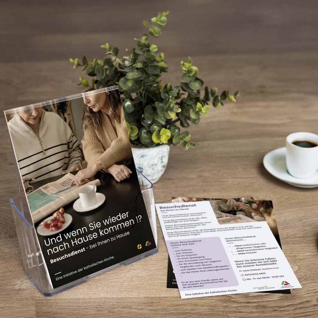 Flyer und Plakat zum kirchlichen Besuchsdienst ausgelegt auf Holztisch – mit emotionalem Bildmotiv, Text und Kaffeetasse